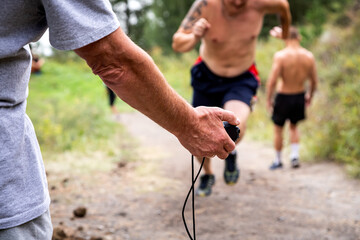Close-up of a trainer holding a stopwatch in his hand and measuring the speed of short-distance running of athletes, in the background beautiful nature
