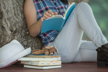  little asian girl reading a book under big tree. children and science. blurred background. learning the imagination and dreams of rural child. studying at home.