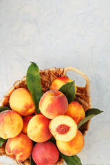 Naklejka na ściany i meble Ripe peaches in a wicker basket on a stone gray table with a juicy peach slice with a stone pit.