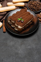 Classic tiramisu dessert on ceramic plate and savoiardi cookies on concrete background