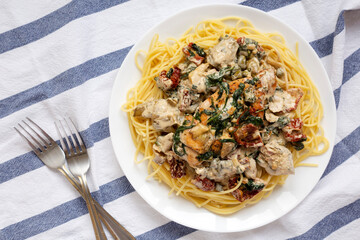 Homemade Creamy Tuscan Chicken with Pasta on a white plate on cloth, top view. Flat lay, overhead, from above.