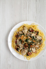Homemade Creamy Tuscan Chicken with Pasta on a white plate on a white wooden background, top view. Copy space.
