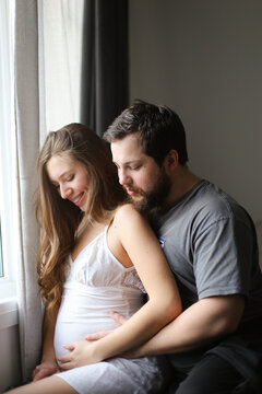Happy american man hugging pregnant woman near window.