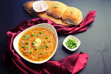 Indian Mumbai Street style Pav Bhaji, garnished with peas, raw onions, coriander and Butter. Spicy thick curry made of out mixed vegetables, served with paav over black background with copy space. 