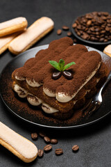 Classic tiramisu dessert on ceramic plate and savoiardi cookies on concrete background