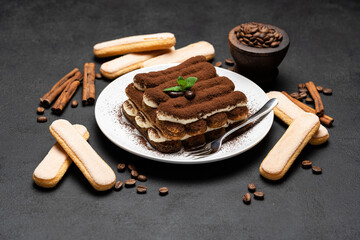 Classic tiramisu dessert on ceramic plate and savoiardi cookies on concrete background