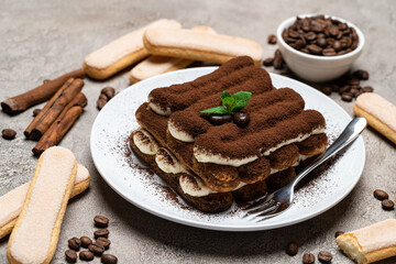 Classic tiramisu dessert on ceramic plate and savoiardi cookies on concrete background