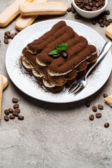 Classic tiramisu dessert on ceramic plate and savoiardi cookies on concrete background