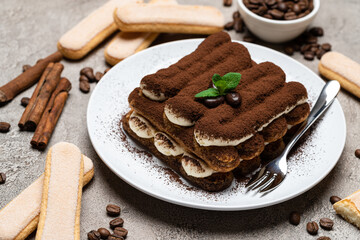 Classic tiramisu dessert on ceramic plate and savoiardi cookies on concrete background