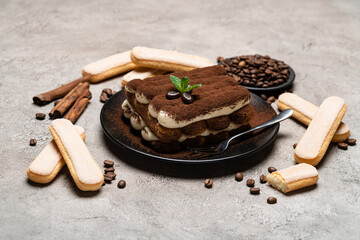 Classic tiramisu dessert on ceramic plate and savoiardi cookies on concrete background