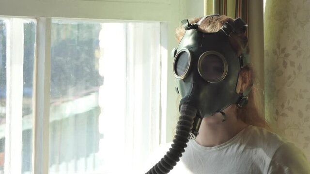 Infection, the Apocalypse. A young woman in a gas mask looks out the window and turns her head. Close-up shooting.