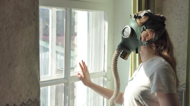 Infection, the Apocalypse. A young woman in a gas mask looks out the window and turns her head. Close-up shooting.