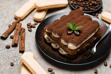 Classic tiramisu dessert on ceramic plate and savoiardi cookies on concrete background