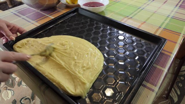 Simple food, pie making. The woman spreads the liquid dough on the baking tray with a spoon, giving it the desired shape for baking.