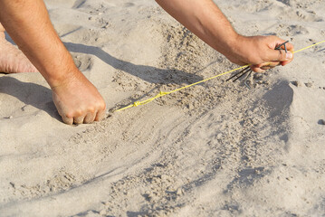 a metal peg driven into the sand to pull the rope out of the tent. Camping on a sandy beach. man raises a tent on the beach. nature travel concept.