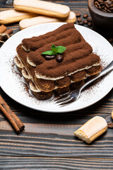 Classic tiramisu dessert on ceramic plate and savoiardi cookies on wooden background