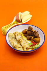 top view of food plate on orange background. in the plate has curry and roti and slice apple served in spoon as side dish.