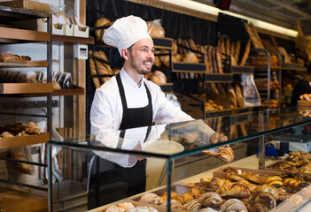 Professional baker is offering fresh tasty croissant in bakery.