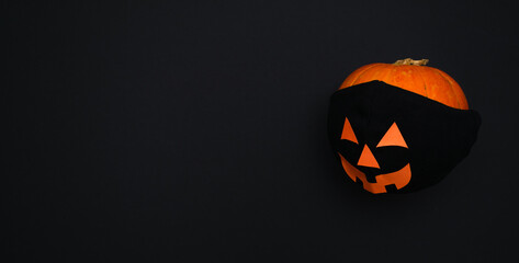 Pumpkin in a black protective mask on a black background.The mask has eyes, mouth and nose made of orange paper.Halloween and covid-19 concept.Copy space for text