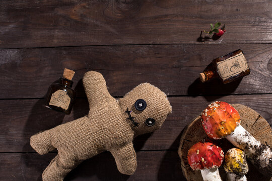 Voodoo doll on a wooden background with dramatic lighting. The concept of witchcraft and black art. A sacking doll on a wooden background and bottles with a poisonous substance and amanita mushrooms.