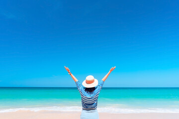 Happy woman raise hand up at tropical beach with blue sky background. Travel vacation and freedom...