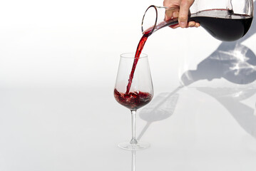Sommelier pours red wine from decanter to wineglass on white background.