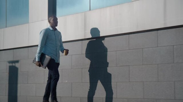 Successful African American business man walks down the street near a business office