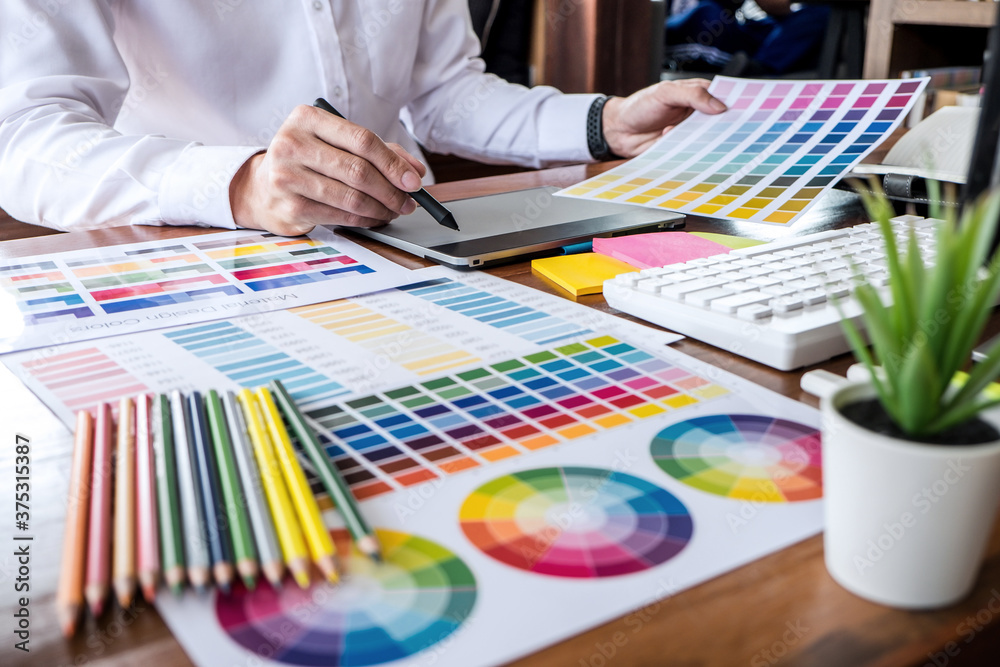 Poster Image of male creative graphic designer working on color selection and drawing on graphics tablet at workplace with work tools and accessories