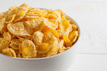 White bowl of cornflakes on a white wooden table.