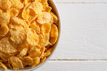 White bowl with cornflakes on a white wooden table. Occupies the left side of the frame.