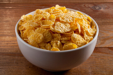 White bowl with cornflakes on a brown wooden table. Bowl in the center of the frame. Horizontal frame.