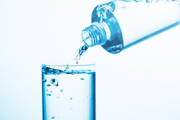 Pouring water from a bottle into glass on a blue background.