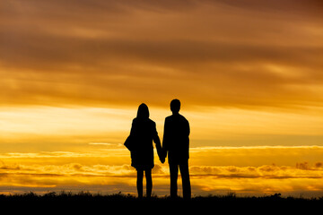 Fototapeta na wymiar 夕陽を背景に手をつなぎ立つ男女のシルエット