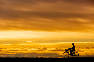 Fototapeta premium 夕陽を背景に自転車通学する男子高校生のシルエット