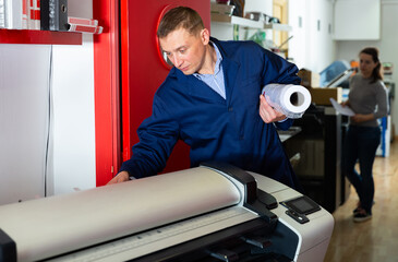 Worker loads new roll of paper into the plotter. High quality photo