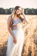 Obraz premium young woman in dress walking in evening in field with hay bales, beautiful romantic girl with long hair outdoors in field