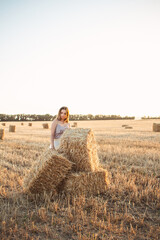Naklejka na ściany i meble young woman lean on haystack walking in summer evening, beautiful romantic girl outdoors in field at sunset