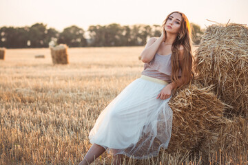 young woman lean on haystack walking in summer evening, beautiful romantic girl outdoors in field at sunset