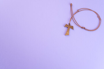 Closeup of a wooden tau cross necklace isolated on a purple background - obrazy, fototapety, plakaty