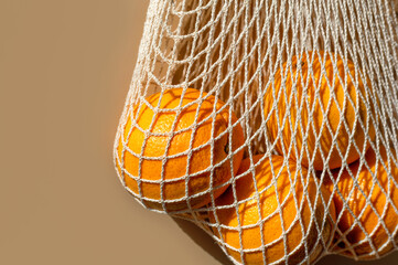 Ripe oranges in a white string bag. Beige background. Close-up. Copy space.