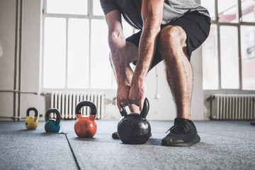 Close up of sportsman lifting kettlebell inside a gym.