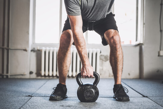 Close up of a fitness man lifting black kettlebell inside a gym.
