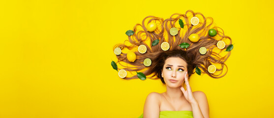 beautiful girl lying on yellow background with citrus fruits in long hair making choice,young woman head thinking