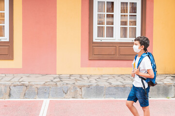 Obraz na płótnie Canvas covid-19, boy with mask and backpack walking to school.