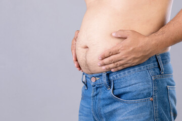 Naklejka premium Fat man standing and show his tummy studio shot on grey background with copy space for text or design. Fat people and healthy concept