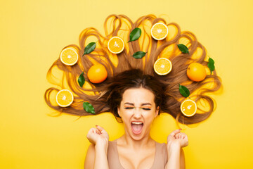Obraz na płótnie Canvas girl lying with orange fruits in long hair screams in despair, young shocked woman with citrus slices and leaves, emotion splash