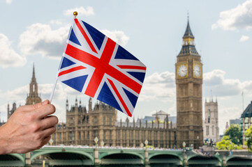 Fototapeta na wymiar Toursist in London holding flag of Great Britain in hand. Big Ben in background.