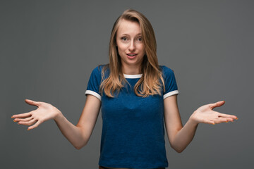 Studio shot of young woman shrugging shoulders looking at the camera being at loss