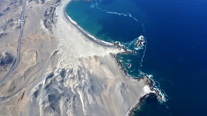 View from above of the dark blue Pacific Ocean, lined with the fine white sand dunes and in the...