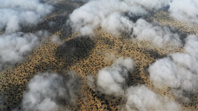 View from above of the white cloud mountains that float deep over the yellow, flat sand desert in Peru between Piura and Chiclayo and cast shadows.